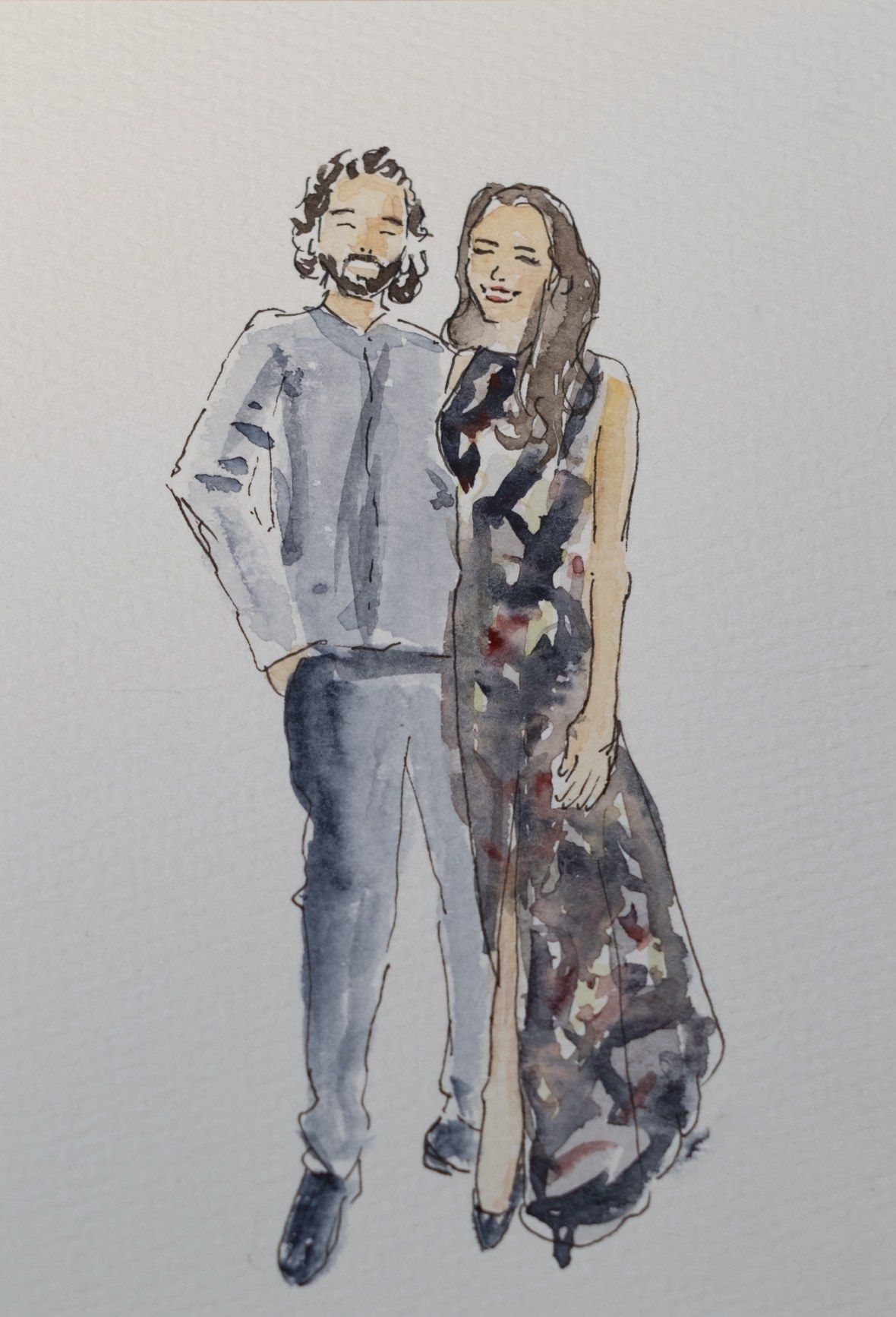 Portrait de couple à l’encre et à l’aquarelle : un homme barbu aux cheveux bouclés en chemise grise, une femme brune en robe longue sombre à motifs, tous deux souriants.